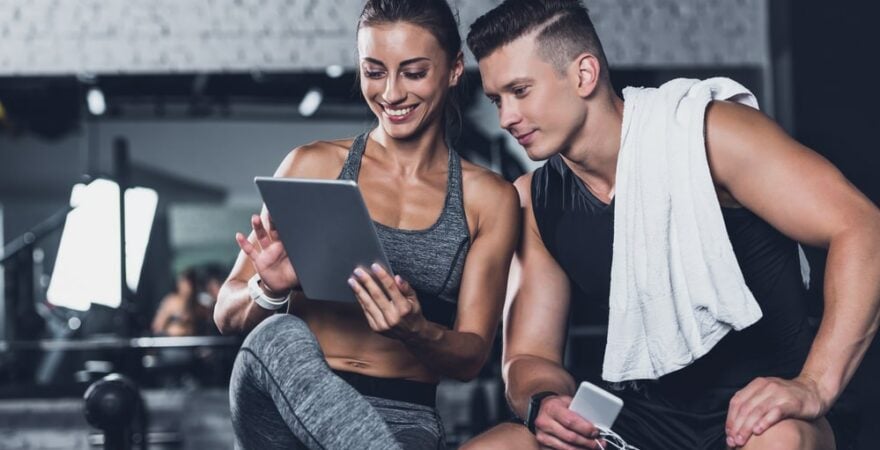 kobieta i mężczna sprawdzają plan treningowy na siłowni