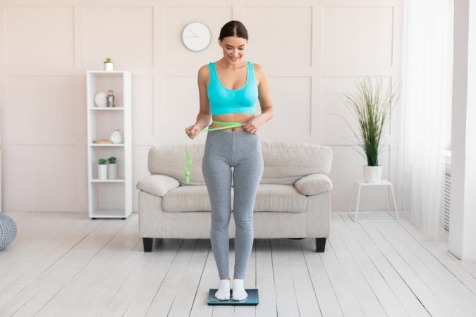 kobieta stoi na wadze i mierzy talię po odchudzaniu